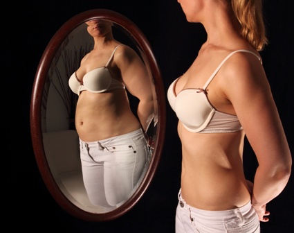 Una chica delgada se mira en un espejo y en el reflejo se ve gorda